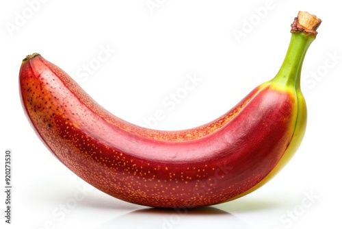 Vibrant red banana with slight green undertones stands upright on a white background, its smooth skin showcasing a few brown spots and gentle curves. photo