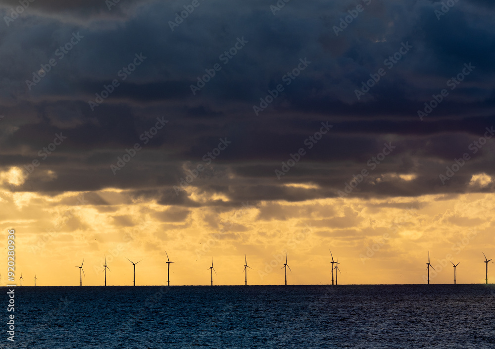 Dark clouds of a thunderstorm over silhouettes of wind turbines in the North sea in the evening sun Dark clouds of a thunderstorm over silhouettes of wind turbines in the North sea in the evening sun