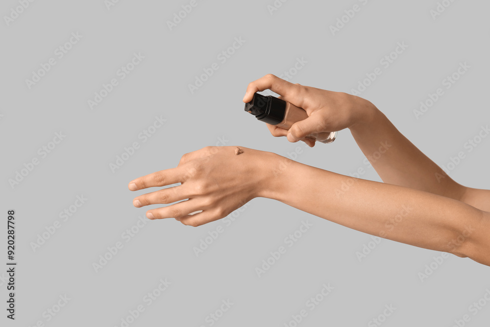 Fototapeta premium Woman applying makeup foundation on grey background