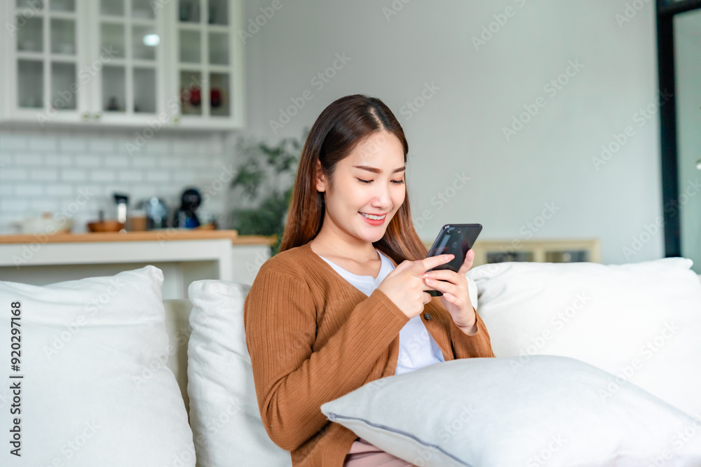 Happy young asian woman relax on comfortable couch at home texting messaging on smartphone, smiling girl use cellphone chatting Happy young asian woman relax on comfortable couch at home texting messaging on smartphone, smiling girl use cellphone chatting