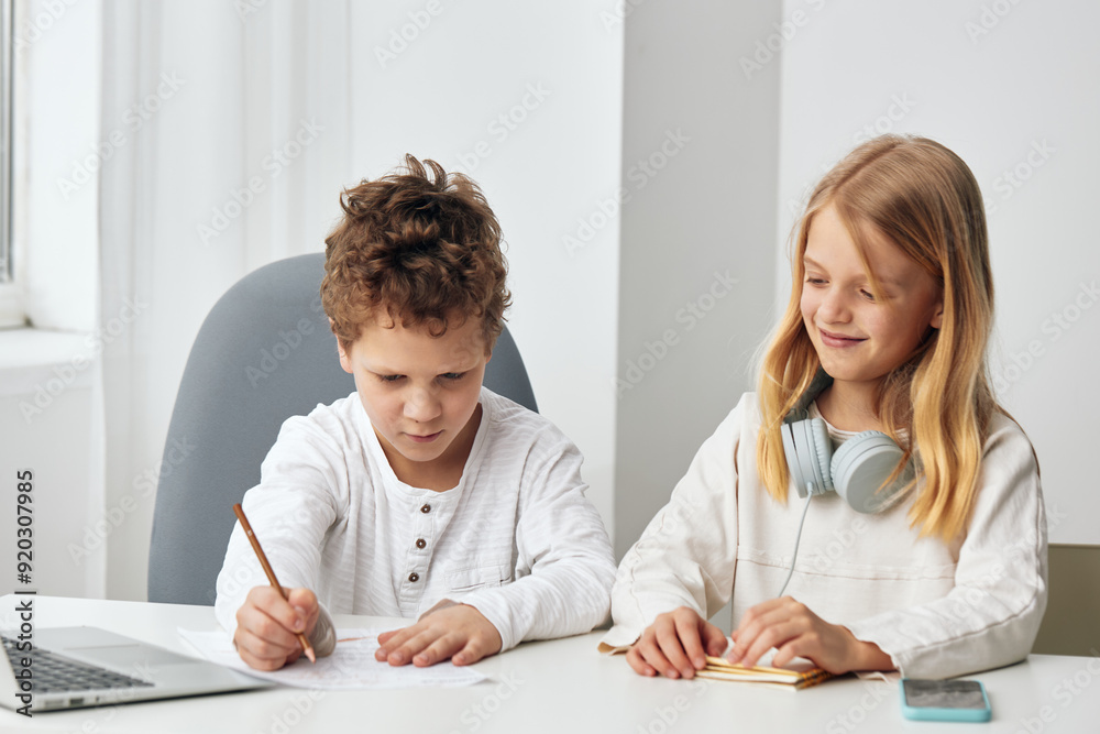 Boy and girl happily studying together at home, using laptops and headphones for online elearning In their cozy living room, they sit at a table with tablets, typing and playing educational games The Boy and girl happily studying together at home, using laptops and headphones for online elearning In their cozy living room, they sit at a table with tablets, typing and playing educational games The