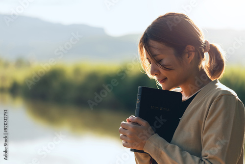 Canvastavla Christian woman praying on the holy bible in a field during a beautiful sunset, holding the bible in her hands