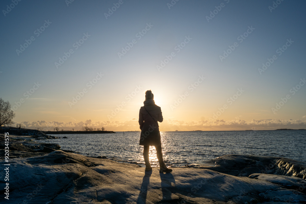 Fototapeta premium lonely blond woman on the beach in Helsinki Finland on a cold winter day watching sunset