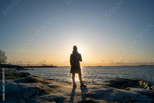 lonely blond woman on the beach in Helsinki Finland on a cold winter day watching sunset