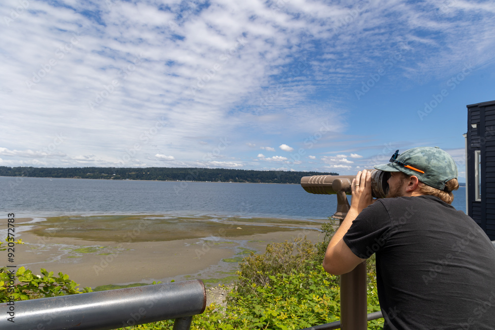 Obraz premium Man using binoculars to view Whidbey Island coastline