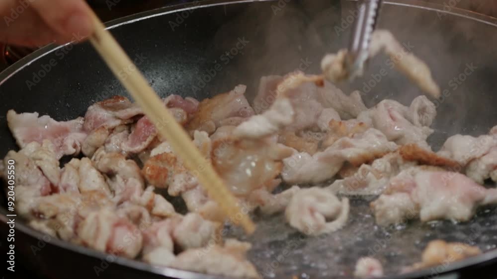 젓가락과 집게를 사용하여 기름을 두른 프라이팬에서 돼지고기를 볶는 모습 젓가락과 집게를 사용하여 기름을 두른 프라이팬에서 돼지고기를 볶는 모습