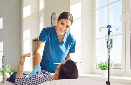 Young female nurse or doctor holding report file with appointment and giving consultation to her male patient lying on the couch in medical clinic and receiving IV drip infusion and vitamin therapy. photo