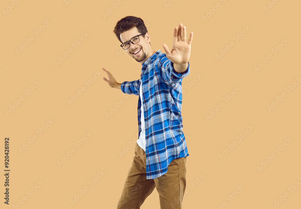 Human gestures and emotions. Cheerful man make stop hand gesture against something, isolated on beige background. Caucasian man in casual clothes spreads his arms to sides and looks at camera smiling.