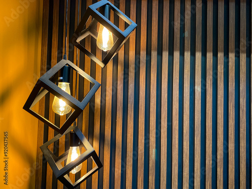 There is a row of squareshaped lights elegantly hanging down from the ceiling, beautifully positioned in front of a charming wooden wall that adds a rustic touch to the ambiance photo