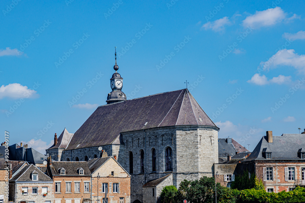 Fototapeta premium Back view of Saint Hilary church surrounded by old buildings against blue sky background, cityscape of Givet town, sunny summer day in Ardennes department, France