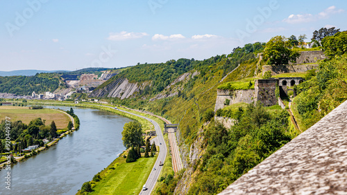 Fototapeta Naklejka Na Ścianę i Meble -  Panoramic view of Meuse river seen from Charlemont fortress, country road and railway tracks stone walls, trees on hill and horizon in background, sunny summer day in the Ardennes department, France