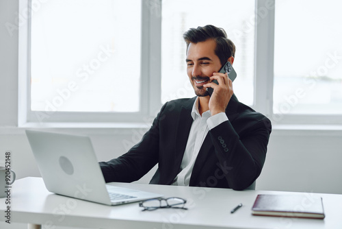 Man in office businessman sitting at desk and working in laptop and talking on phone, modern suit, finance and startup concept and data analysis, working lifestyle in bright office.