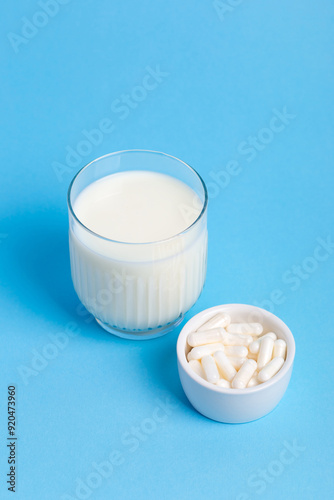 Many lactase tablets in small white plate and a glass of milk containing lactose on a blue background. lactase tablets for assimilation of lactose from dairy products. Lactose intolerance. photo