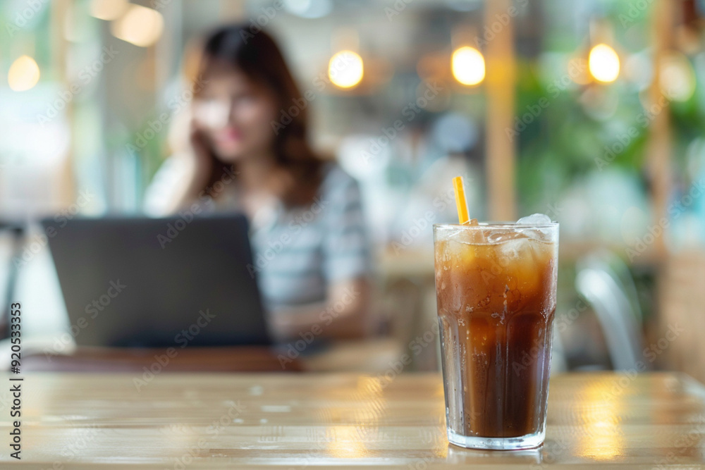 Place to work for freelancer co-working cafe relaxing summer altosphere concept. Coffee iced beverage drink with straw on cafe restaurant table with woman working on laptop on background. Place to work for freelancer co-working cafe relaxing summer altosphere concept. Coffee iced beverage drink with straw on cafe restaurant table with woman working on laptop on background.