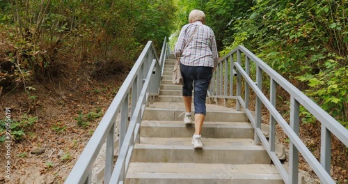 An elderly woman climbs up a long staircase in a park.