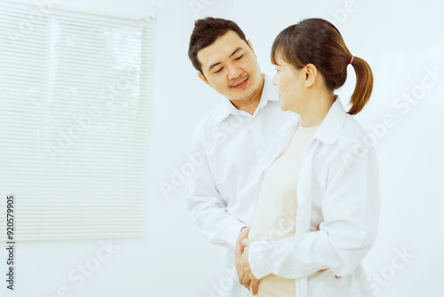 A middle-aged Asian couple, with the woman being pregnant, shares a loving embrace, smiling with happiness and anticipation for their soon-to-arrive baby, symbolizing family togetherness and joy.