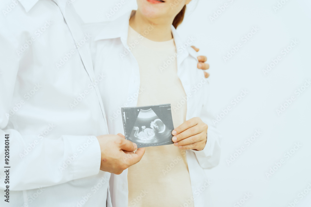 A middle-aged Asian couple, with the woman being pregnant, shares a loving embrace, smiling with happiness and anticipation for their soon-to-arrive baby, symbolizing family togetherness and joy. A middle-aged Asian couple, with the woman being pregnant, shares a loving embrace, smiling with happiness and anticipation for their soon-to-arrive baby, symbolizing family togetherness and joy.