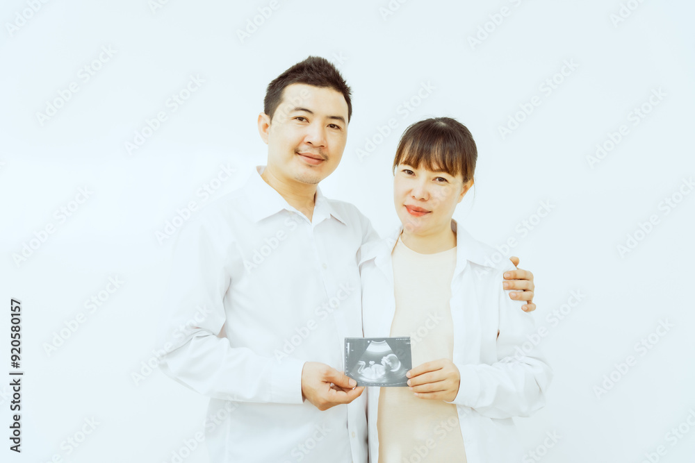 A middle-aged Asian couple, with the woman being pregnant, shares a loving embrace, smiling with happiness and anticipation for their soon-to-arrive baby, symbolizing family togetherness and joy. A middle-aged Asian couple, with the woman being pregnant, shares a loving embrace, smiling with happiness and anticipation for their soon-to-arrive baby, symbolizing family togetherness and joy.