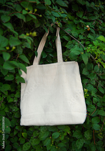 White canvas tote bag mockup template with long handles among the green plant leaves outdoor photo