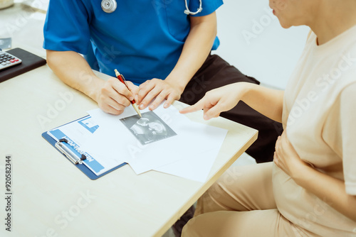 A male Asian pediatrician in a white lab coat conducts a prenatal checkup for a middle-aged pregnant woman, focusing on maternal and fetal health, offering expert care and guidance. photo