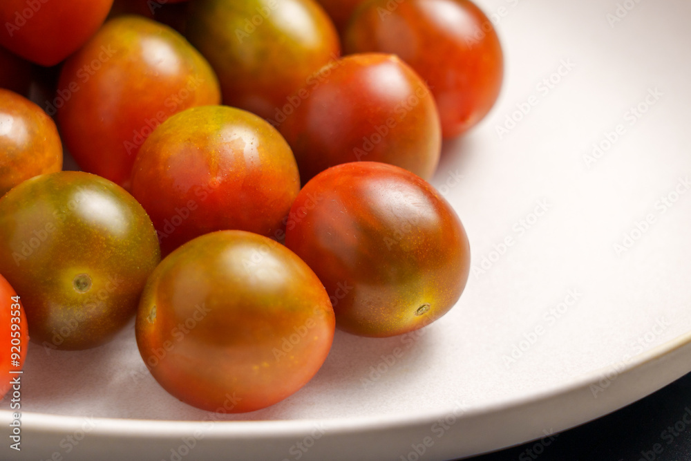 Freshly picked kumato cherry tomatoes on a ceramic plate close up. Vegetable organic ingredients. Top view. Freshly picked kumato cherry tomatoes on a ceramic plate close up. Vegetable organic ingredients. Top view.