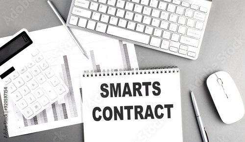 Smart contract text on a notebook surrounded by a keyboard, mouse, calculator, and financial documents on a gray desk