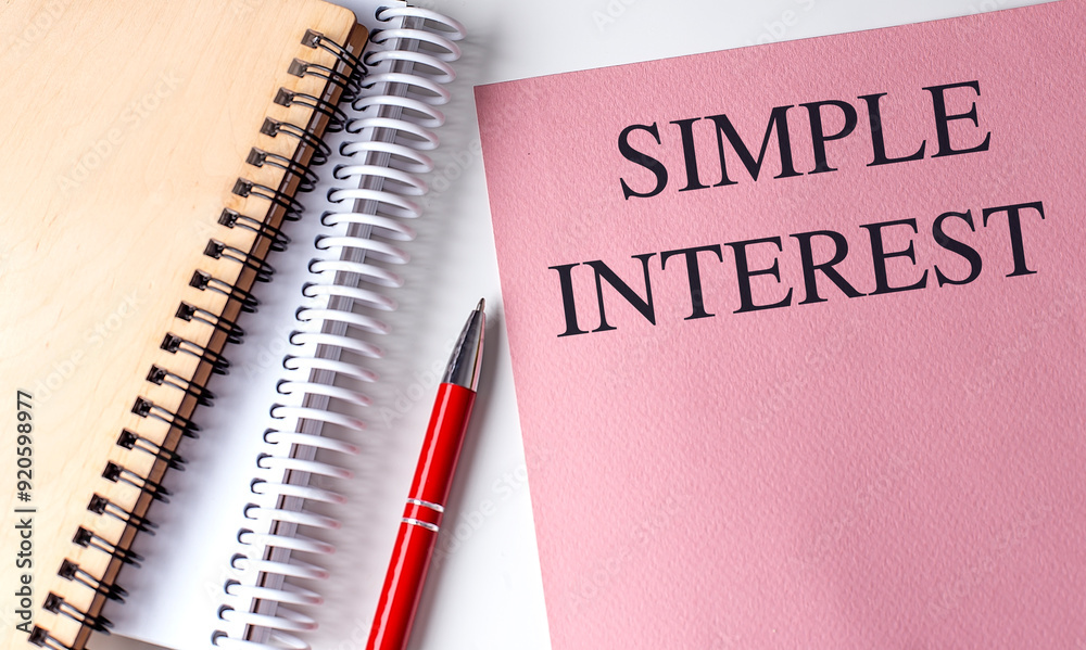 Simple interest text on a pink notebook with a red pen and spiral-bound notepads