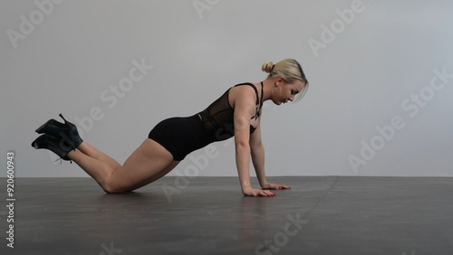 Young woman in black clothes warming up before dance rehearsal high hills in a white room with a black floor