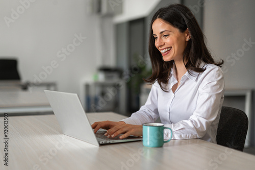 Beautiful brunette working on lap top and having a cup of coffee and smiling