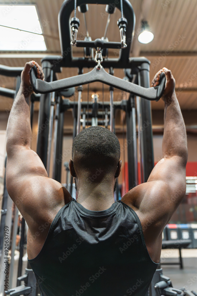 Fototapeta premium Muscular black man training back in the gym with pulleys