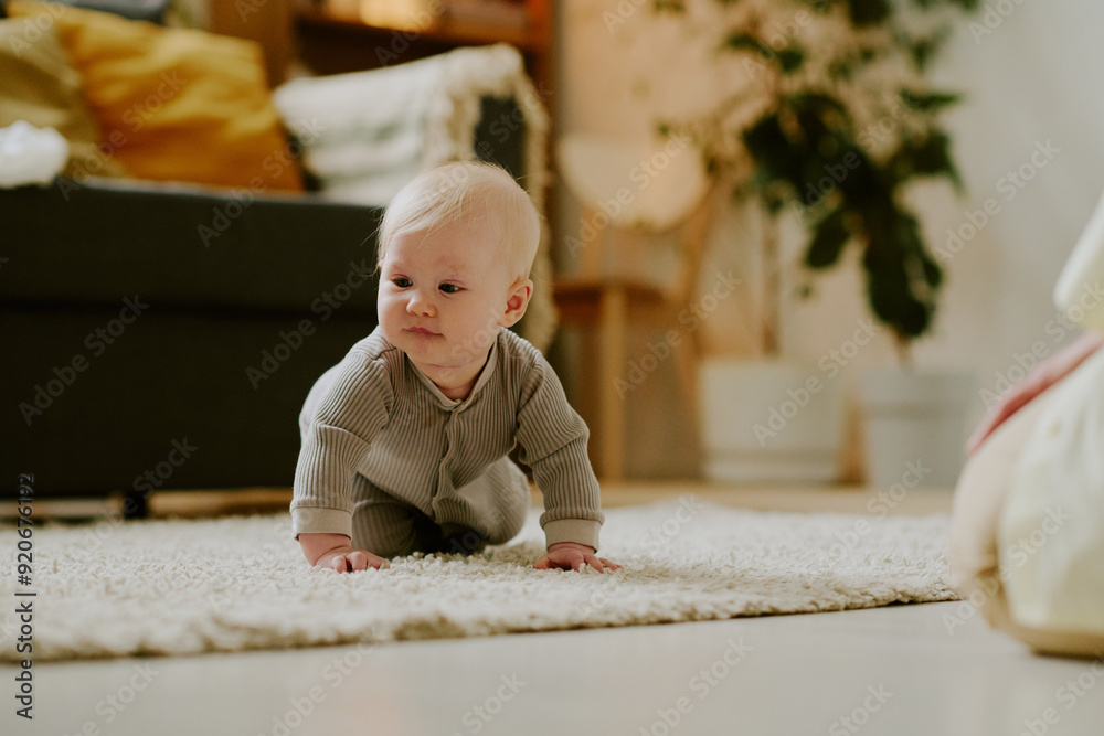 Baby wearing neutral-colored outfit crawling on soft carpet in cozy living room setting, surrounded by furniture and plants creating a warm, inviting atmosphere