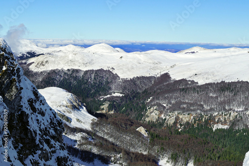 Winter landscape from the top of Troglava in the Biogradska Gora National Park (Montenegro): view of coniferous and deciduous forests, snow-capped mountain slopes and peaks with clouds lying on them.