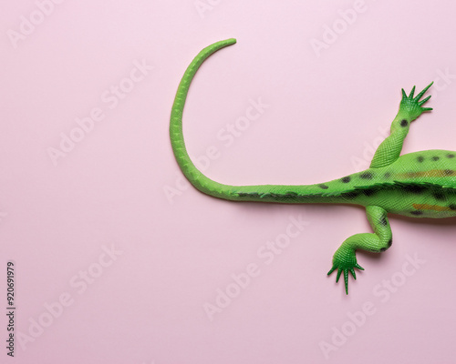 Tail of green lizard toy on pastel pink background. Minimal art concept.