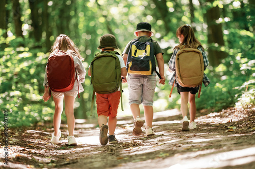 With backpacks. Kids in forest at summer daytime together