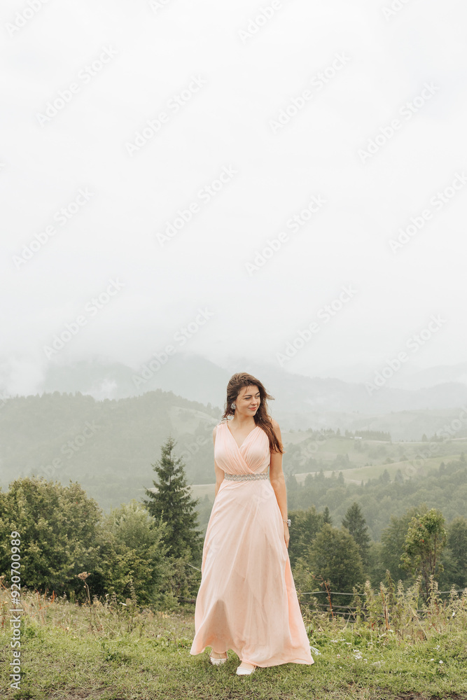 Obraz premium A woman in a pink dress stands on a grassy hillside overlooking a mountain range