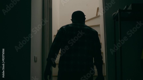 Slow motion of a man in a striped shirt, cap and holding a pistol walking up stairs. Concept of burglary, trespassing, murder.