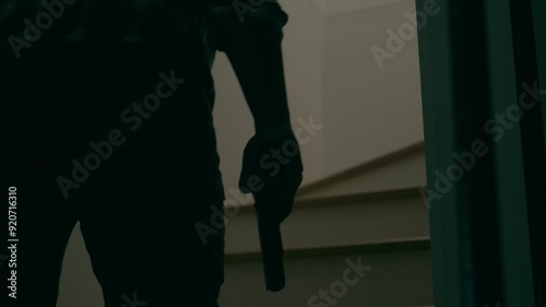 Slow motion of a man in a striped shirt, cap and holding a pistol walking up stairs. Concept of burglary, trespassing, murder.