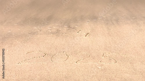 The concept of the New Year. The text of 2025, handwritten on a sandy surface. The figures of 2024 were washed away by the sea wave. We welcome the year 2025. Happy New Year. Seashore, waves, sand.