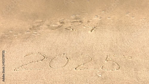 The concept of the New Year. The text of 2025, handwritten on a sandy surface. The figures of 2024 were washed away by the sea wave. We welcome the year 2025. Happy New Year. Seashore, waves, sand.