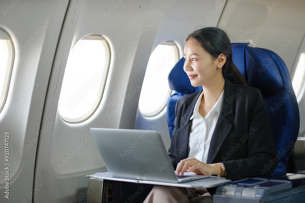 A woman is sitting in an airplane seat with a laptop open in front of her A woman is sitting in an airplane seat with a laptop open in front of her