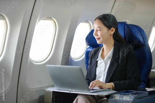 A woman is sitting in an airplane seat with a laptop open in front of her