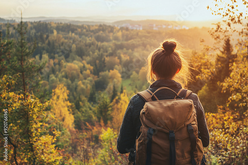 Rear view of female traveler with backpack looking out over the scenic walk in the autumn forest or spring nature during the evening with the setting sun. photo