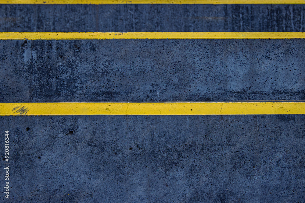 Fototapeta premium Closeup of a textured asphalt road with weathered yellow stripes on a rough gray pavement, great for use in street photography, urban design, or traffic-related visuals. Copy space 