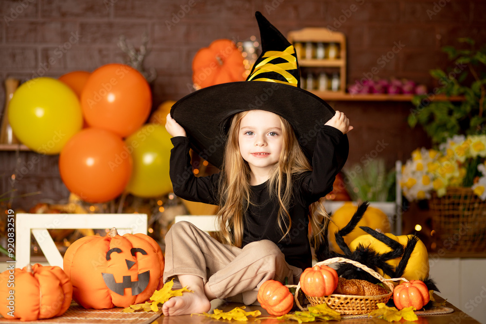 halloween, a cute smiling child girl in a witch costume in a dark kitchen with pumpkins and a big spider and festive decor during the Halloween celebration rejoices halloween, a cute smiling child girl in a witch costume in a dark kitchen with pumpkins and a big spider and festive decor during the Halloween celebration rejoices