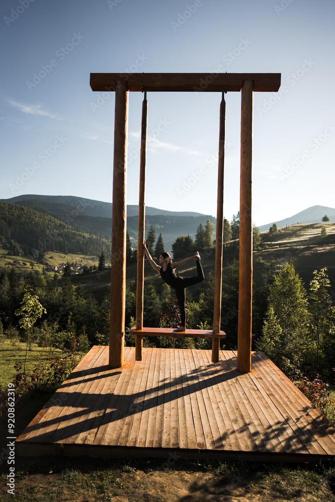A young woman does yoga on a swing against the background of the mountains. Yoga and meditation concept A young woman does yoga on a swing against the background of the mountains. Yoga and meditation concept