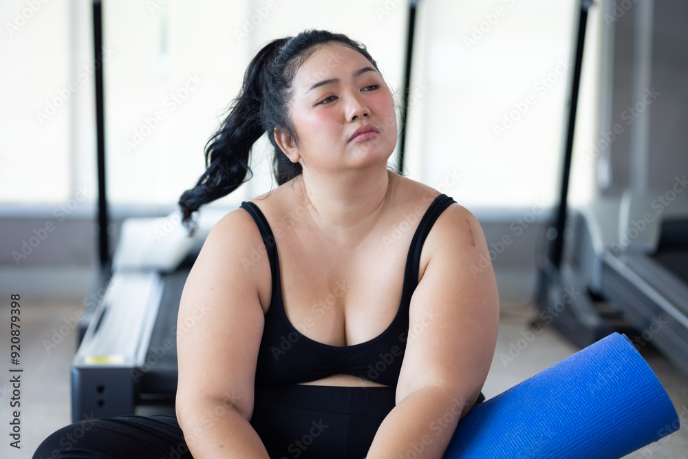 Fototapeta premium Tired fat asian woman. beautiful young chubby overweight woman wearing sporty fitness clothes doing exercise indoors at gym fitness sport club, body and health care