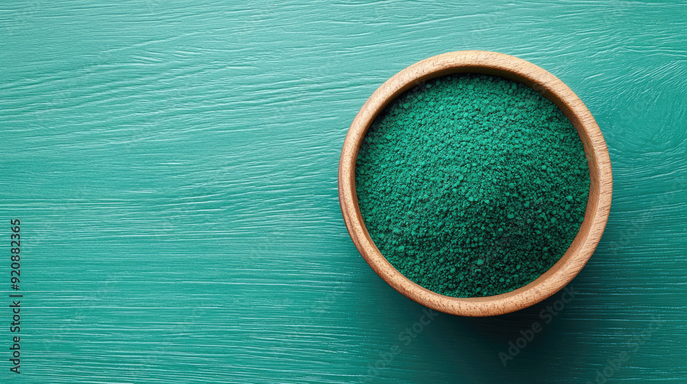 A close-up view of green powder in a wooden bowl on a vibrant turquoise background, highlighting natural colors and textures. A close-up view of green powder in a wooden bowl on a vibrant turquoise background, highlighting natural colors and textures.