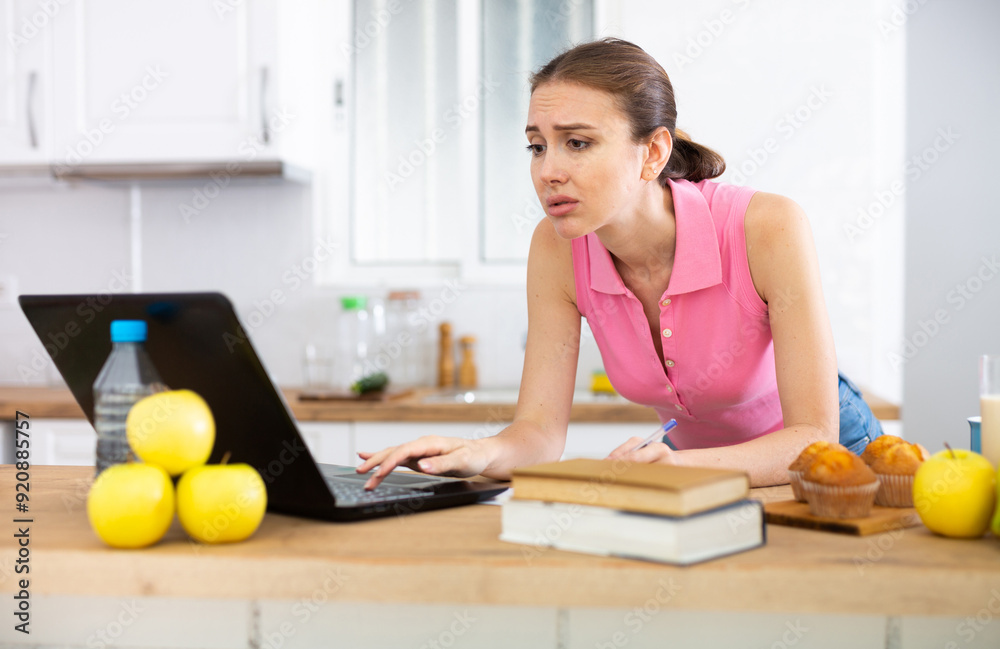 Emotional woman using laptop for work or study in home kitchen Emotional woman using laptop for work or study in home kitchen