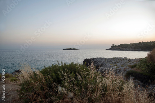 Inlet with islet and cliffs covered with Mediterranean scrub during a summer sundown. Marina di Camerota, Salerno, Italy.