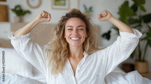 A woman in a white print pajama set is sitting up in bed with her arms raised in a triumphant gesture, showing a broad smile and a sense of achievement.